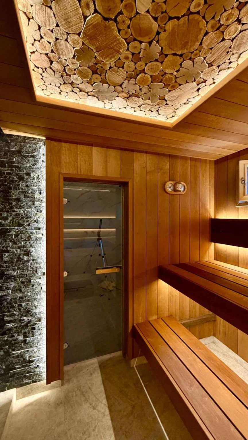 Finished sauna with illuminated wood-slice ceiling, layered benches and glass door