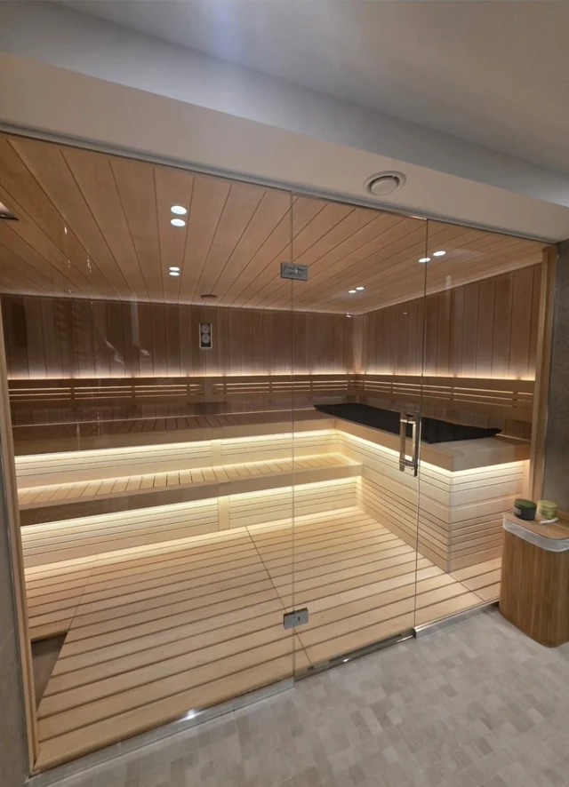 Glass-front sauna with illuminated tiered wood benches and an L-shaped upper seating area