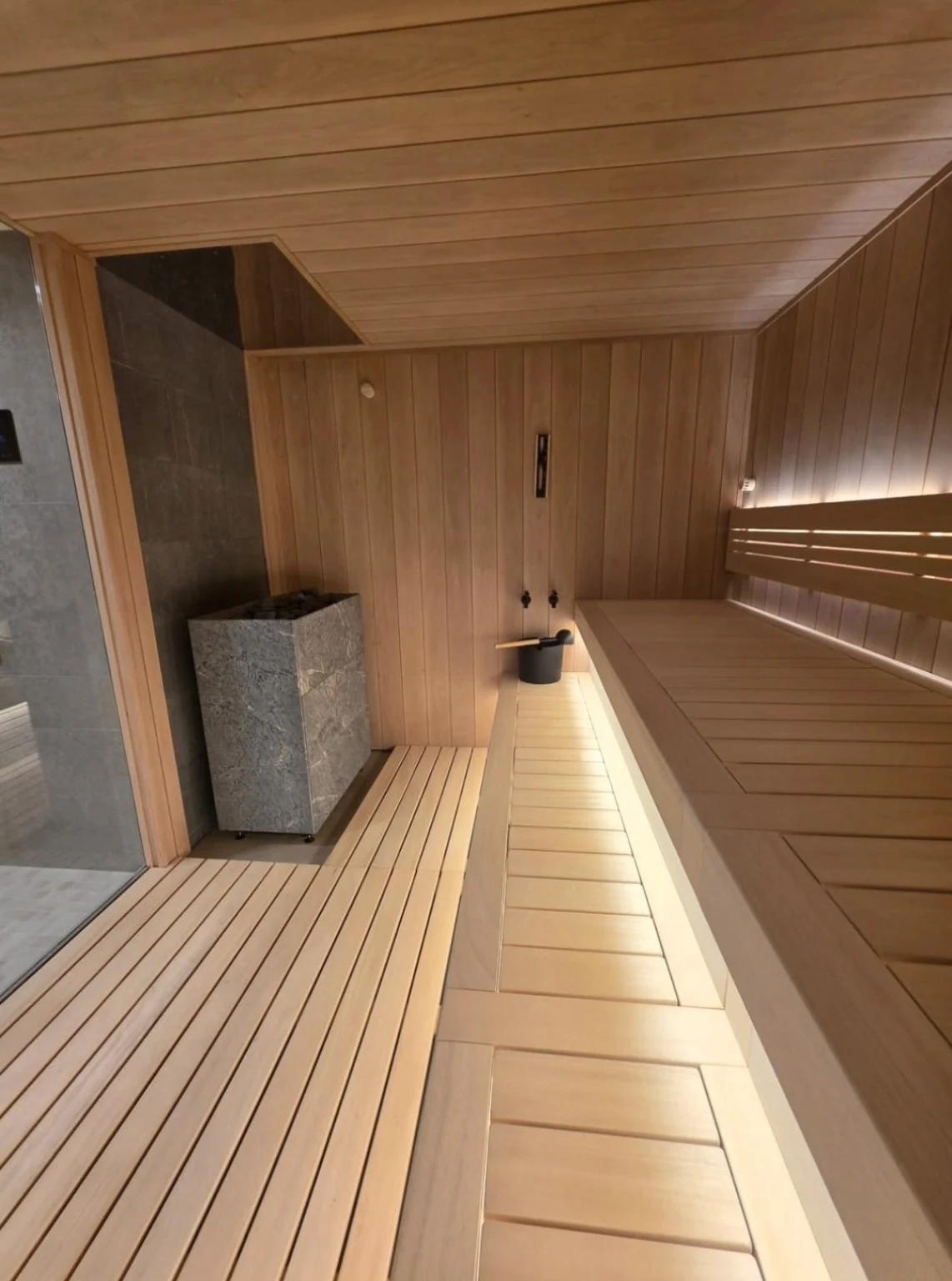 Stone-clad sauna heater beside a wood floor platform and illuminated bench steps
