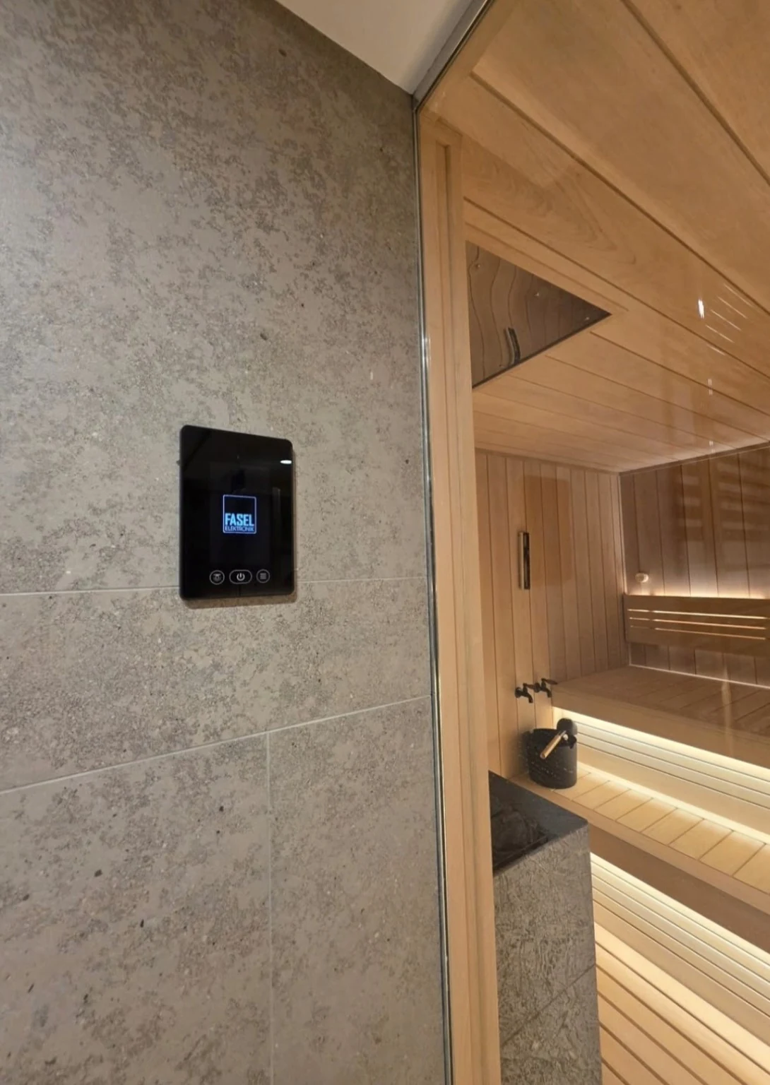 Wall-mounted FASEL controller beside the glass sauna front