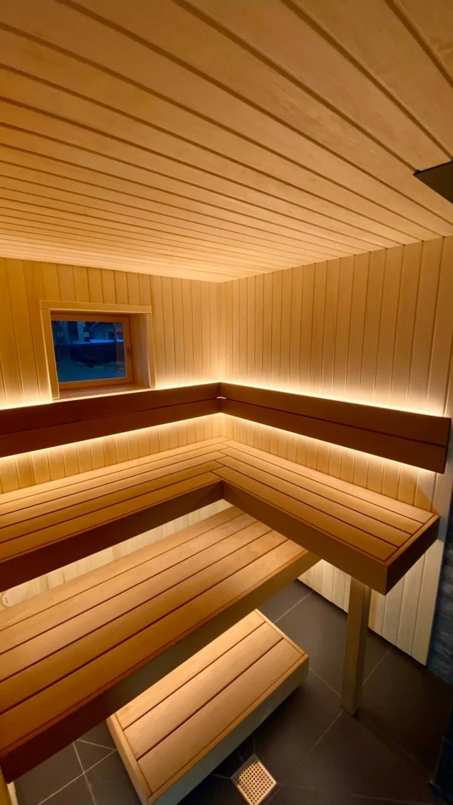 Finished sauna with wraparound benches, dark backrests and warm lighting