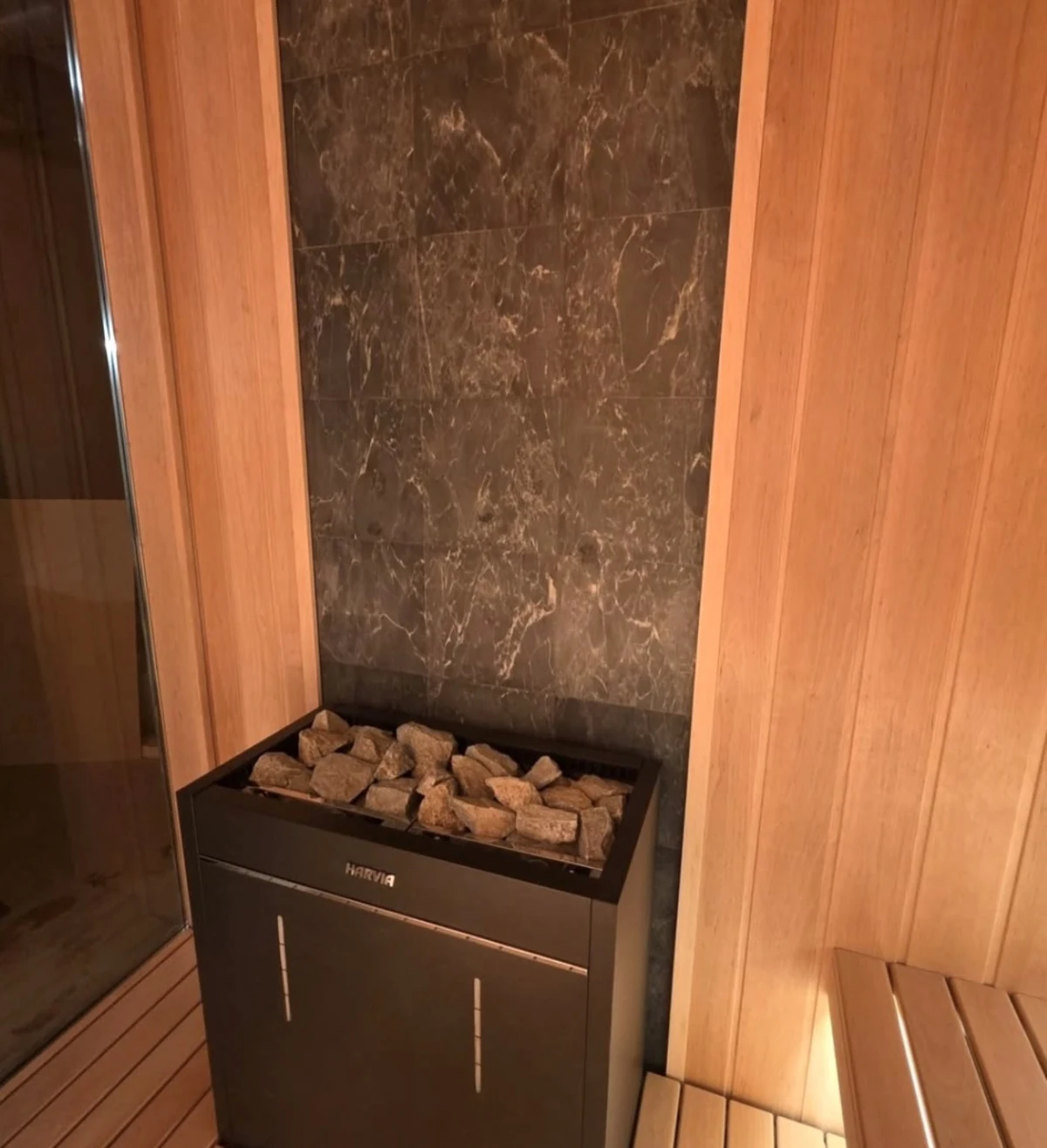 HARVIA electric sauna heater with stones in front of a dark tile feature wall