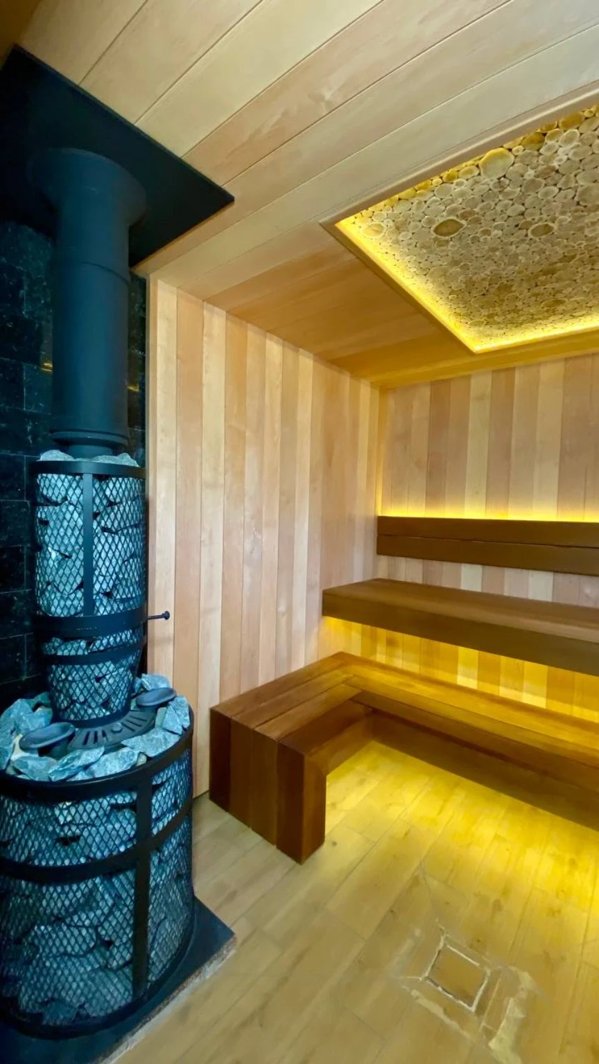 Finished sauna with wood-burning heater, illuminated ceiling panel and tiered benches